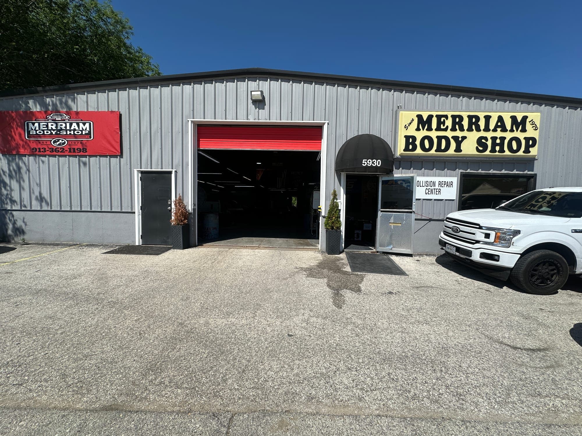 Front of the Merriam Body Shop building on Merriam Drive, with the open bay door and the shop sign